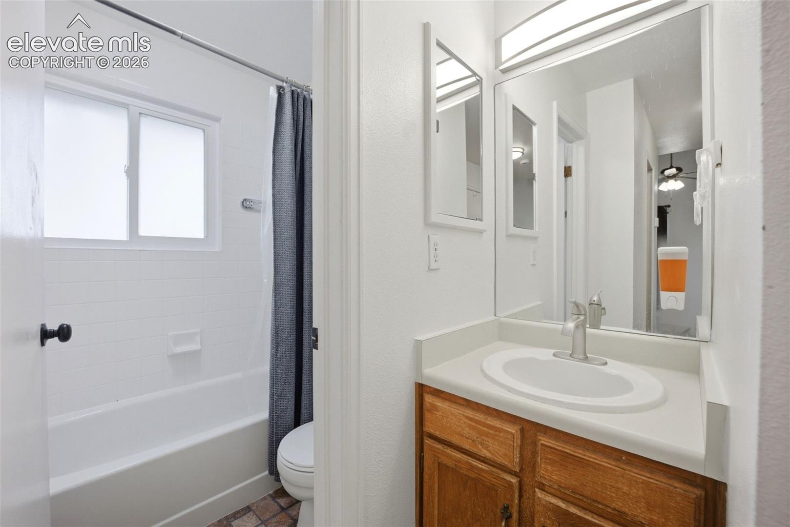 Bathroom featuring a wood-finish vanity with a solid-surface countertop, an integrated sink with a polished chrome faucet, a wall-mounted vanity mirror, and a tub-shower combination with tile surround