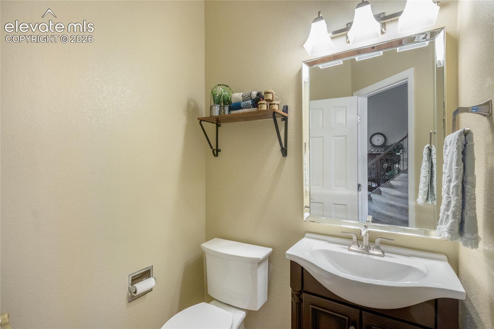 Dark wood vanity with a white integrated sink basin, chrome-finish faucet, rectangular wall-mounted mirror, and three-bulb vanity lighting fixture