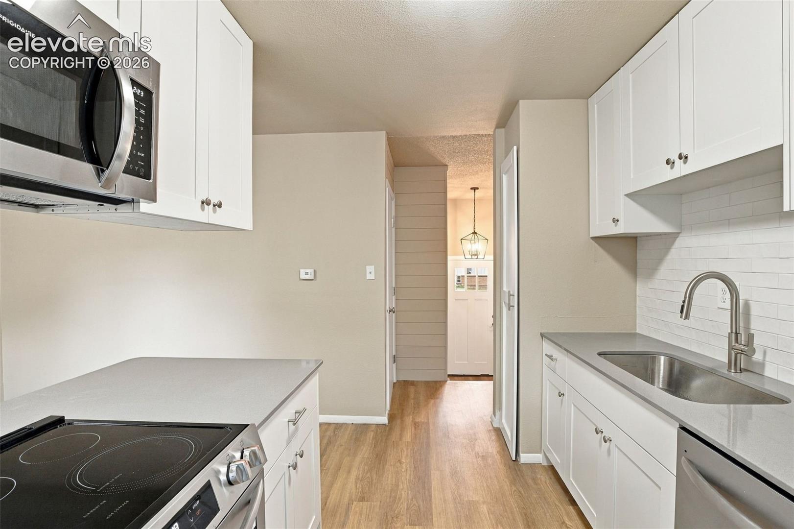 Kitchen featuring white shaker-style cabinetry, solid-surface countertops, a subway tile backsplash, stainless steel appliances, and wood-finish flooring