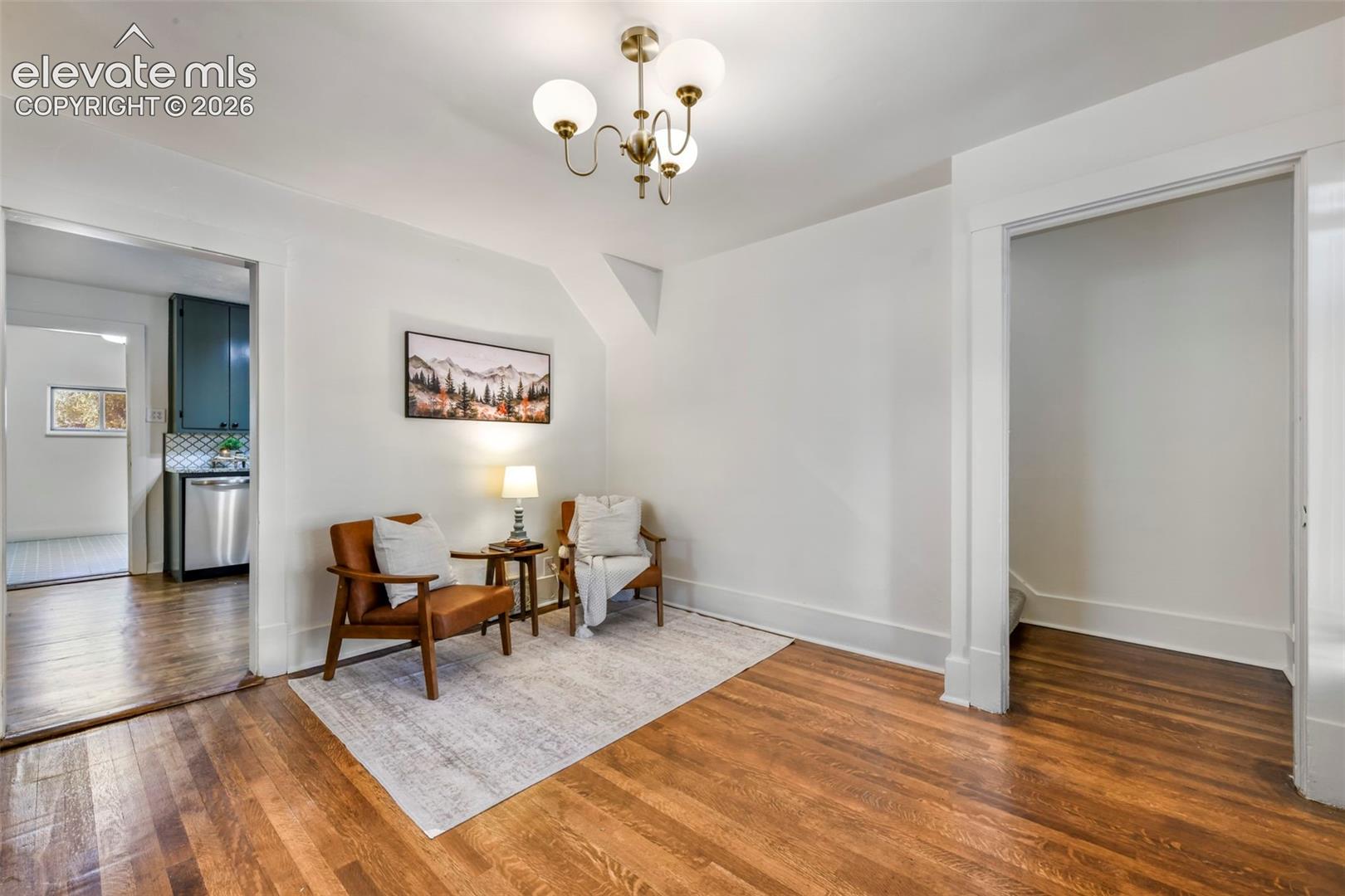 Wood-finish flooring throughout, bright white wall finishes, and a classic multi-arm chandelier with glass globes