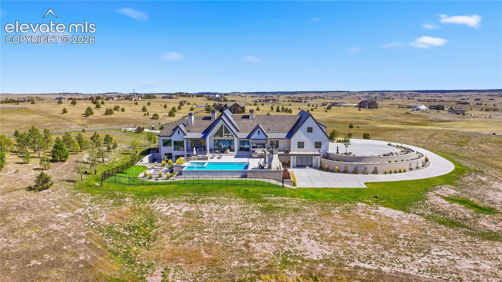 Custom residence featuring multi-gabled rooflines, stone and siding exterior, expansive rear patio, integrated pool with spa, and a circular concrete driveway