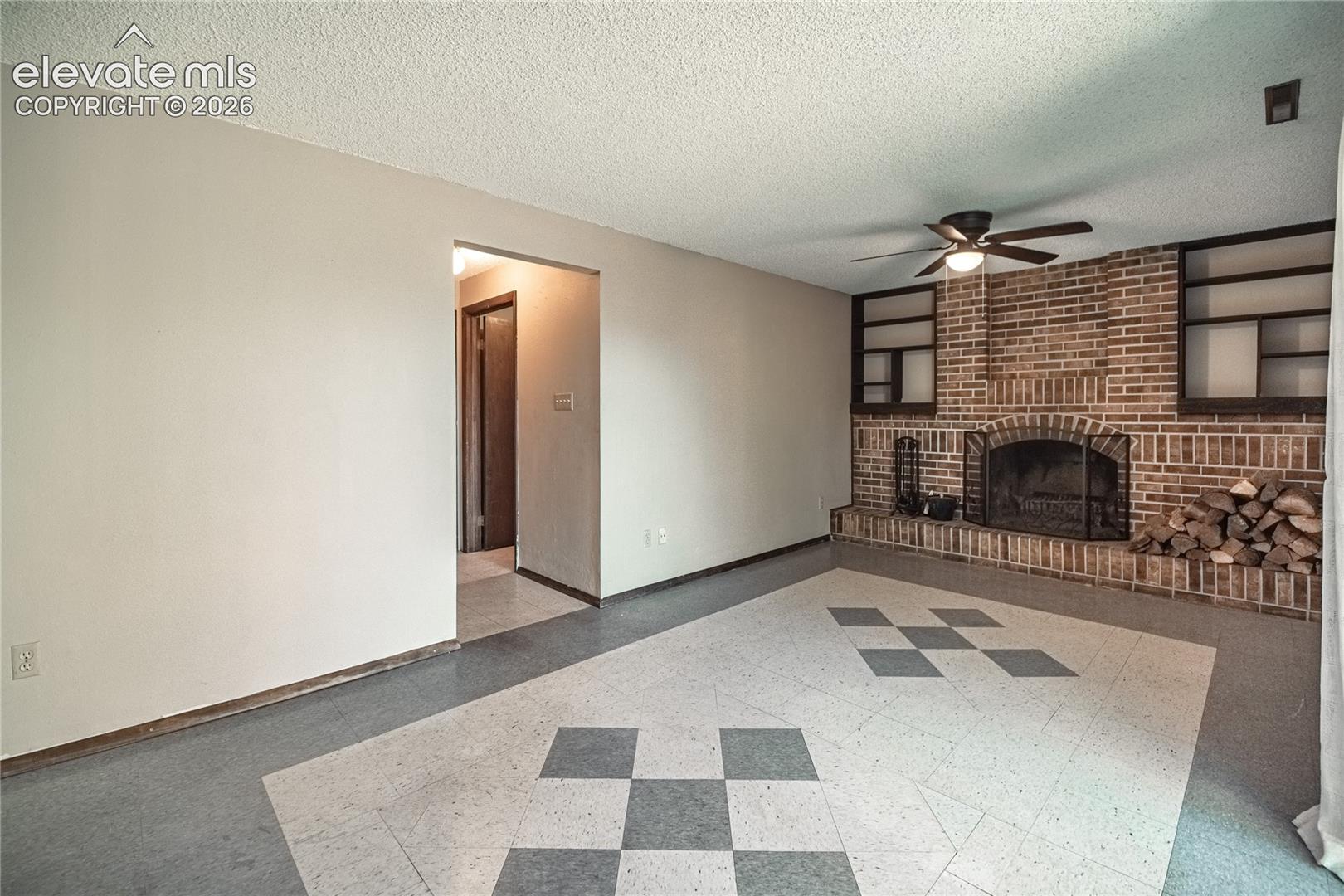 Floor-to-ceiling brick fireplace with integrated shelving, patterned tile flooring, and a ceiling-mounted light fixture with fan