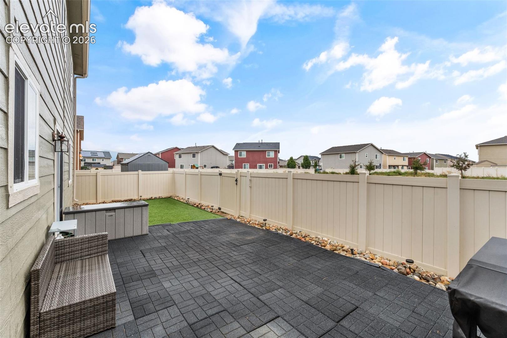 Fenced backyard featuring a paver patio, artificial turf, and decorative rock landscaping