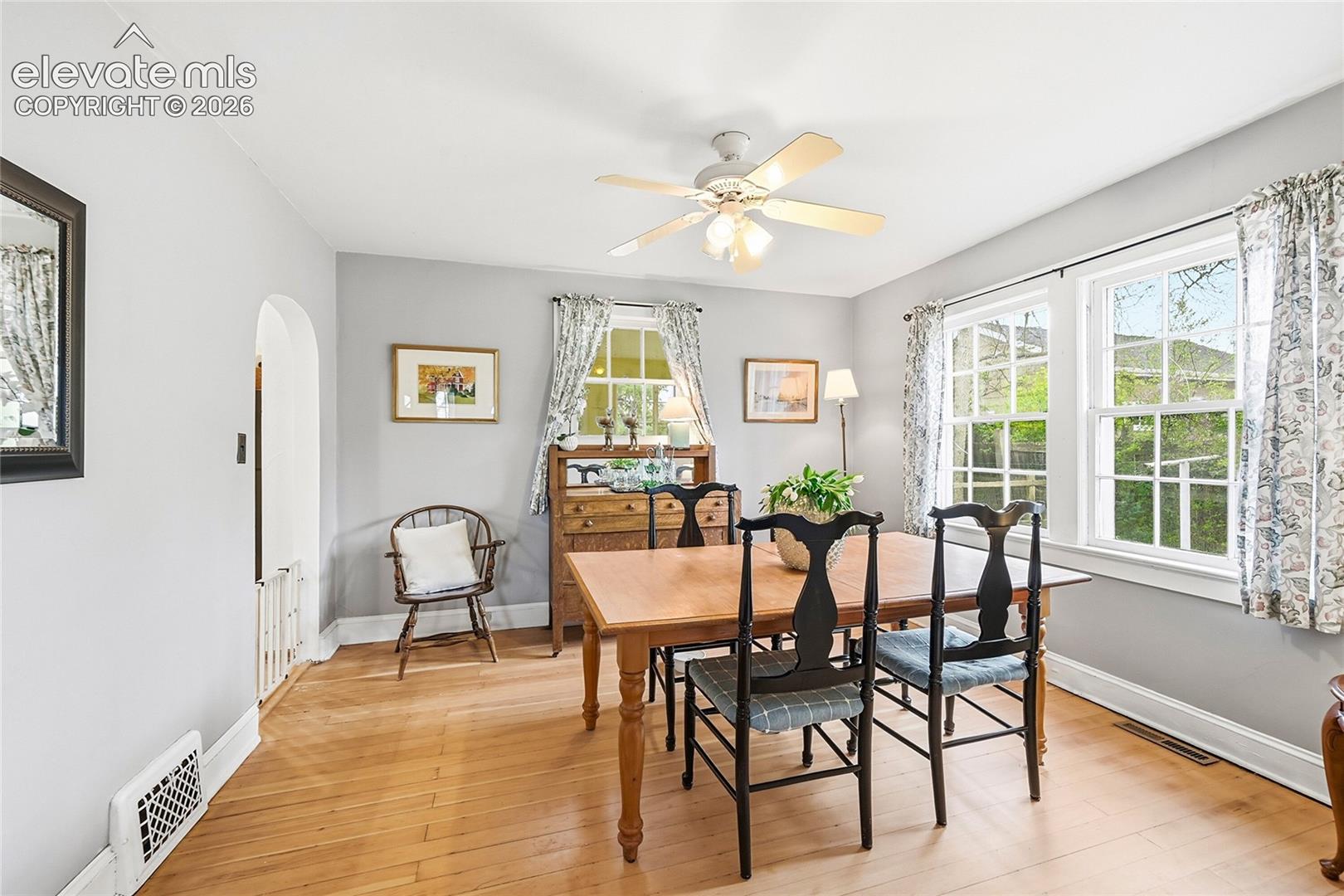 Interior space featuring wood-finish flooring, an arched entryway, double-hung windows, and a ceiling-mounted light fixture with a central fan