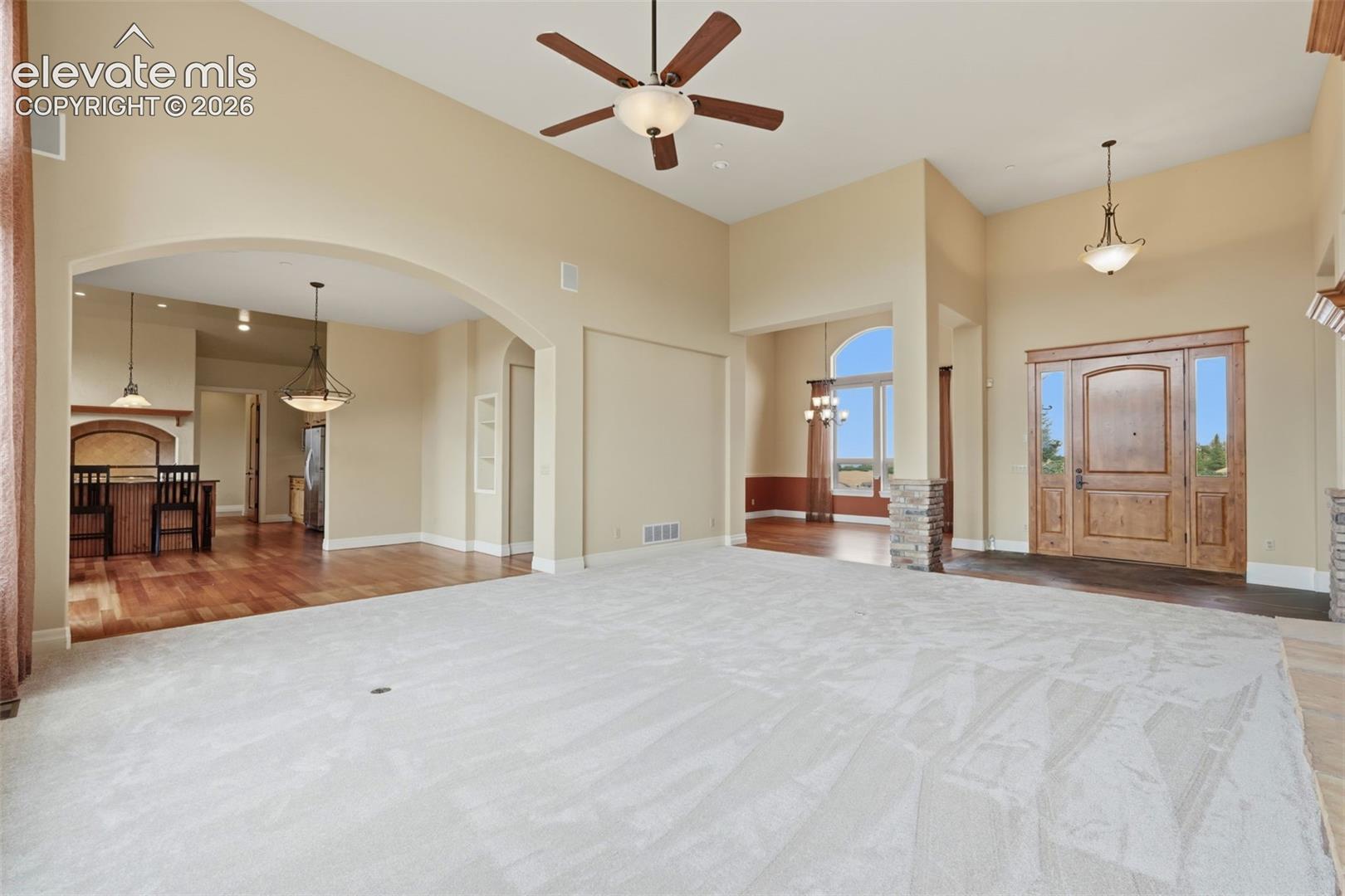 Spacious interior featuring a grand entryway with a solid wood door and sidelights, high ceilings with a ceiling fan, arched doorways, and a combination of light-colored carpeting and wood-finish flooring