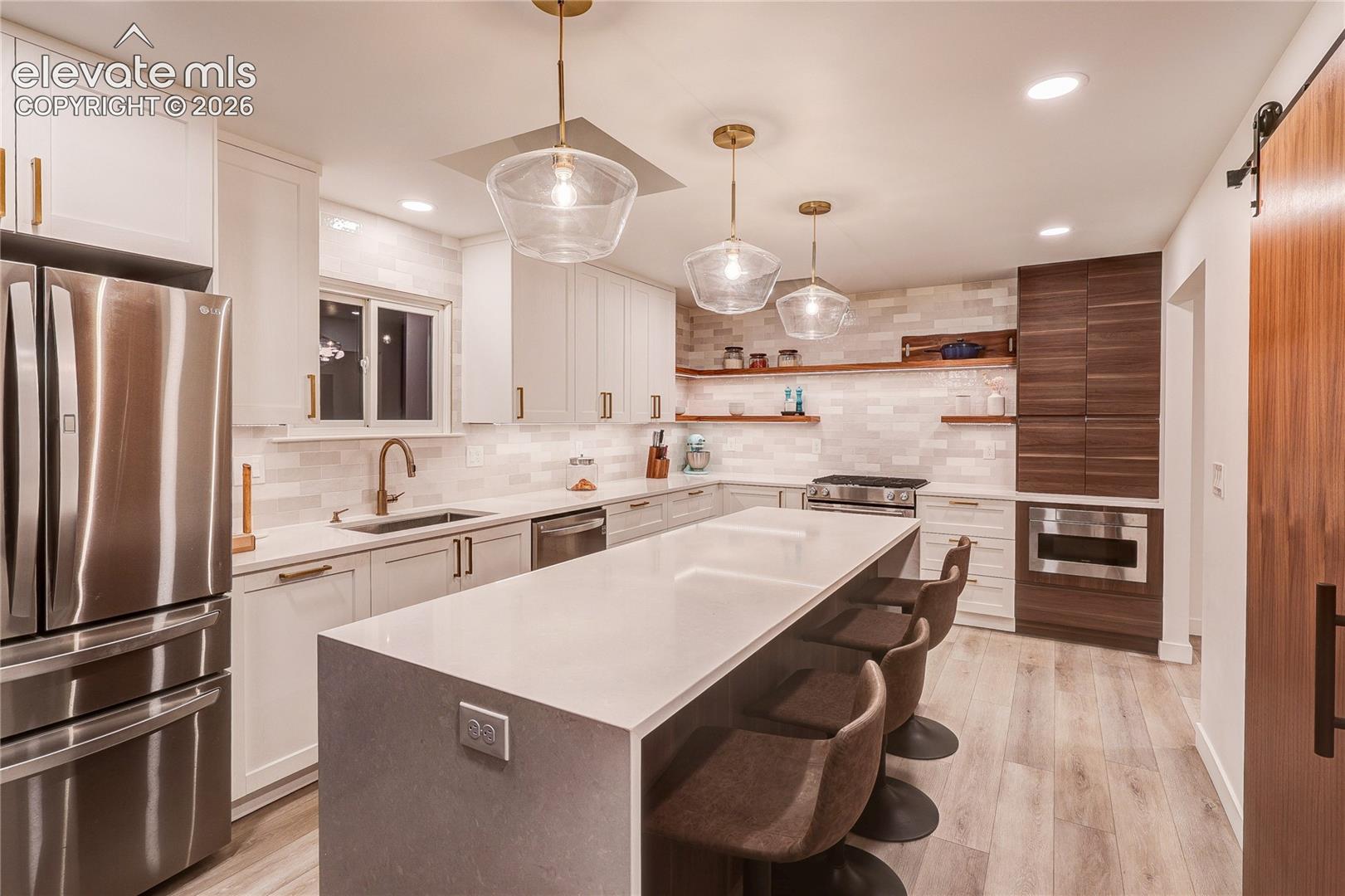 Contemporary kitchen featuring a large center island, white cabinetry, integrated stainless steel appliances, a tile backsplash, and wood-finish flooring