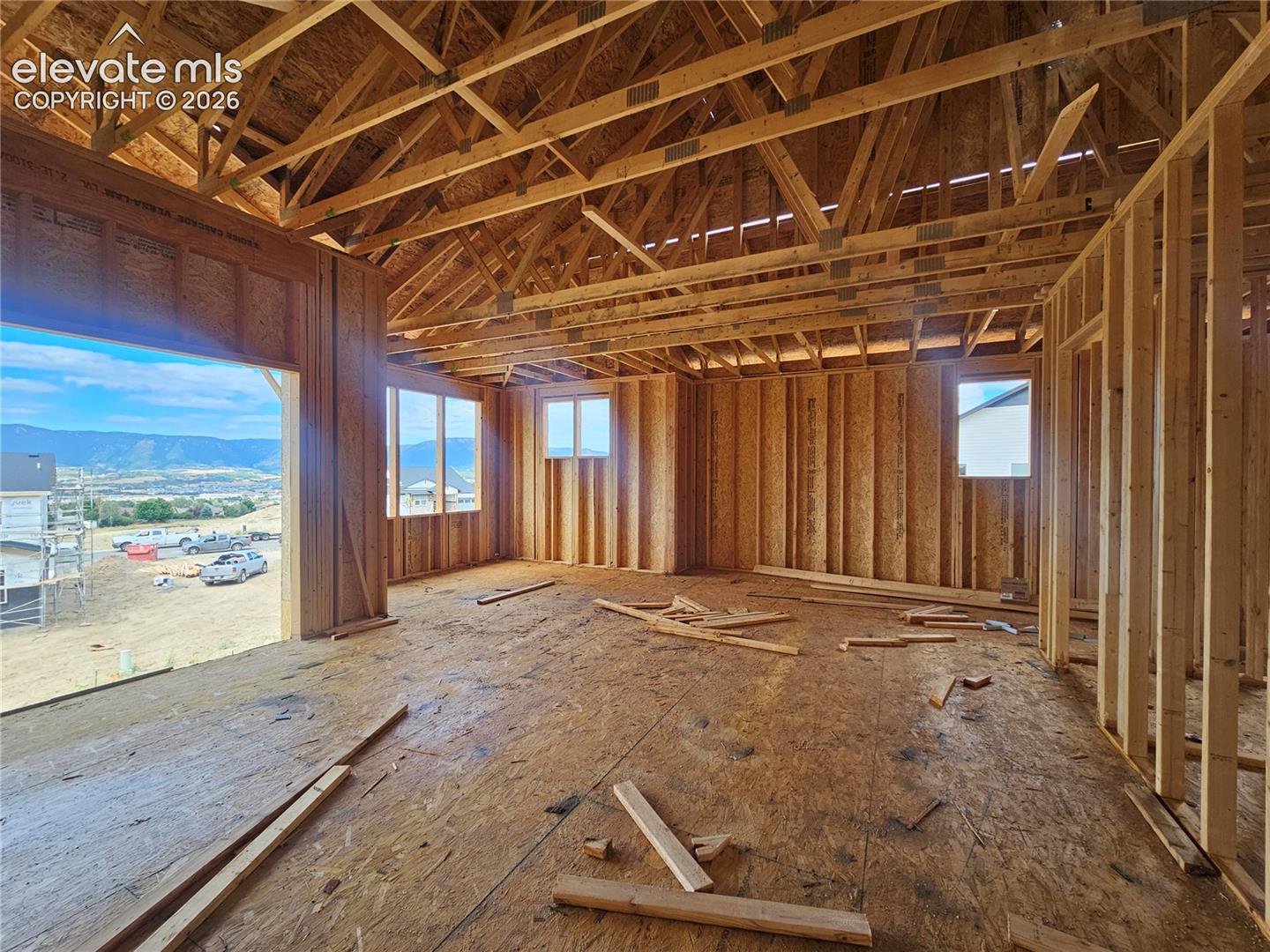 living room with exposed wood framing and vaulted open truss ceiling, large framed opening with distant mountain view