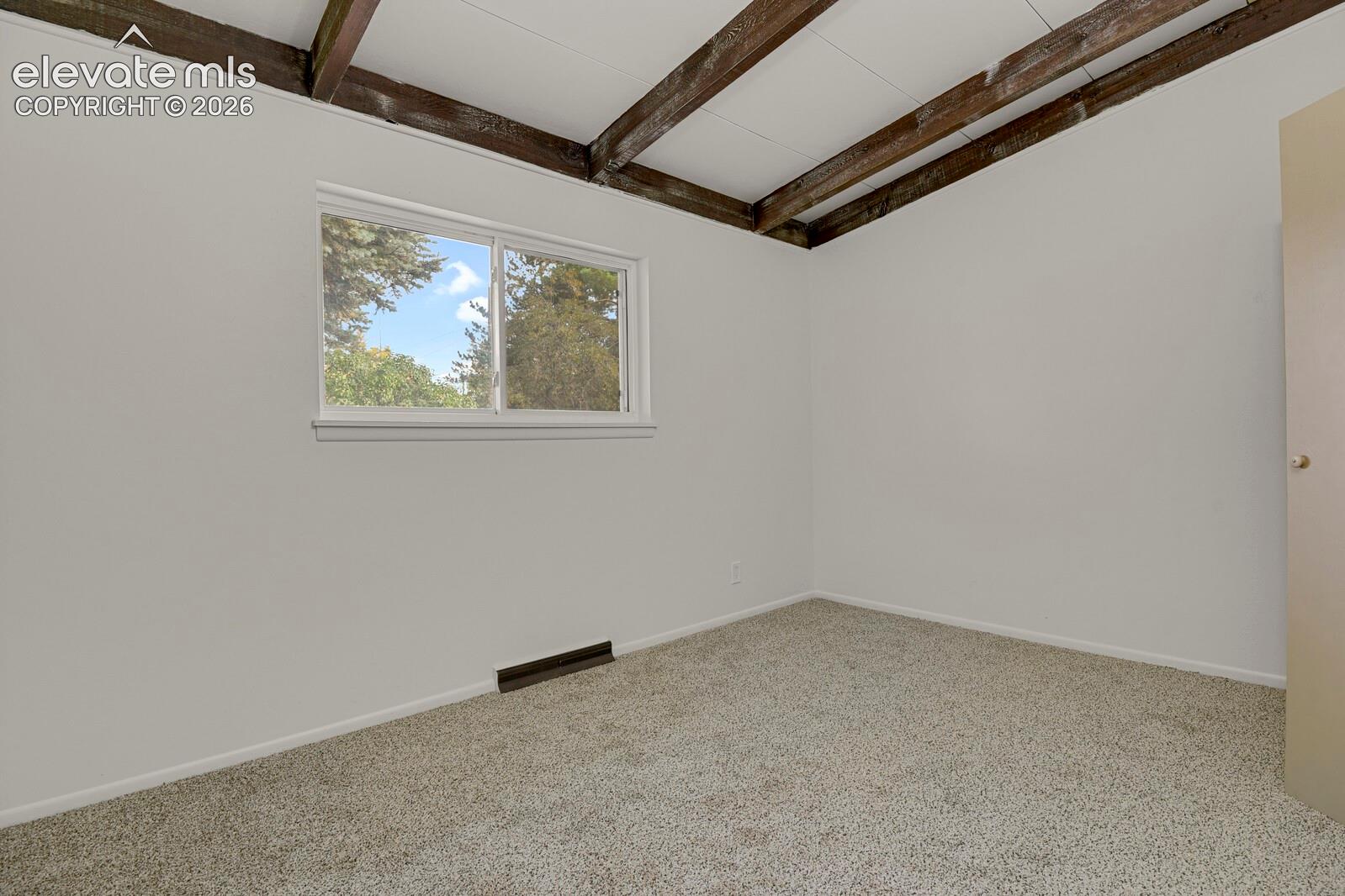 Bedroom featuring exposed ceiling beams, neutral carpeting, and a horizontal sliding window