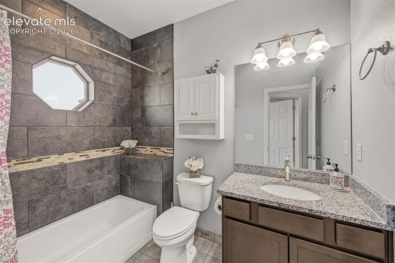 Guest bathroom featuring granite countertop, shower-tub combination with tile walls and a whimsical octagonal window