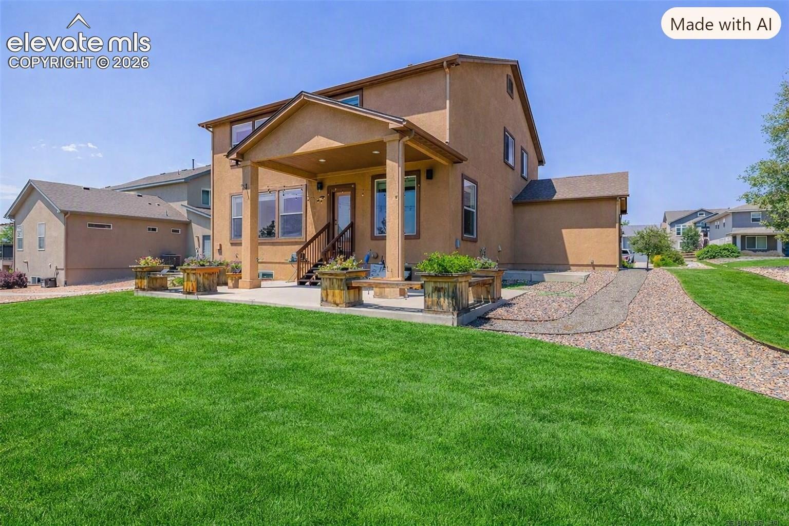 Stucco exterior featuring a covered rear patio, integrated concrete terrace, manicured lawn, and gravel pathway