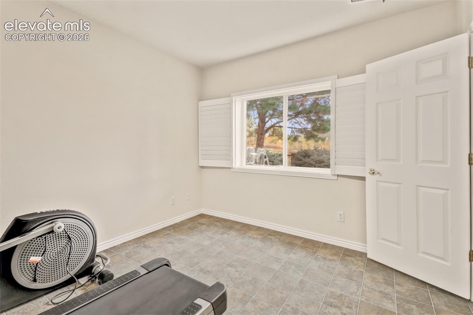Neutral interior room featuring tile flooring, a large sliding window with white plantation shutters, and a six-panel interior door