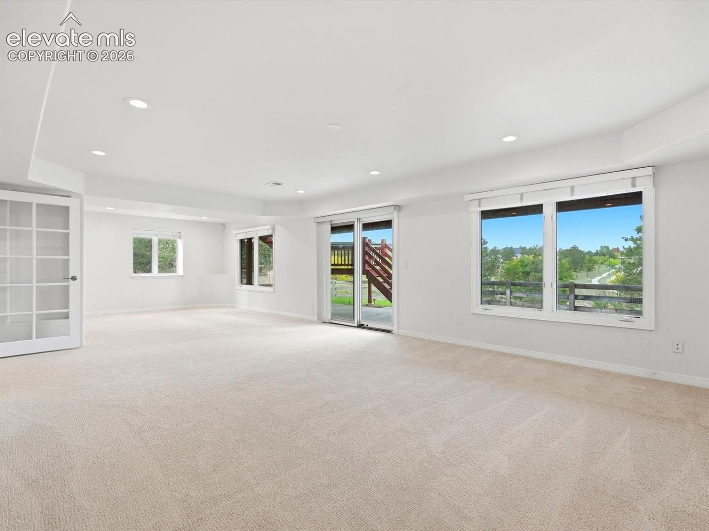 Open interior space featuring neutral carpeting, recessed ceiling lighting, sliding glass patio doors, large windows, and white French doors