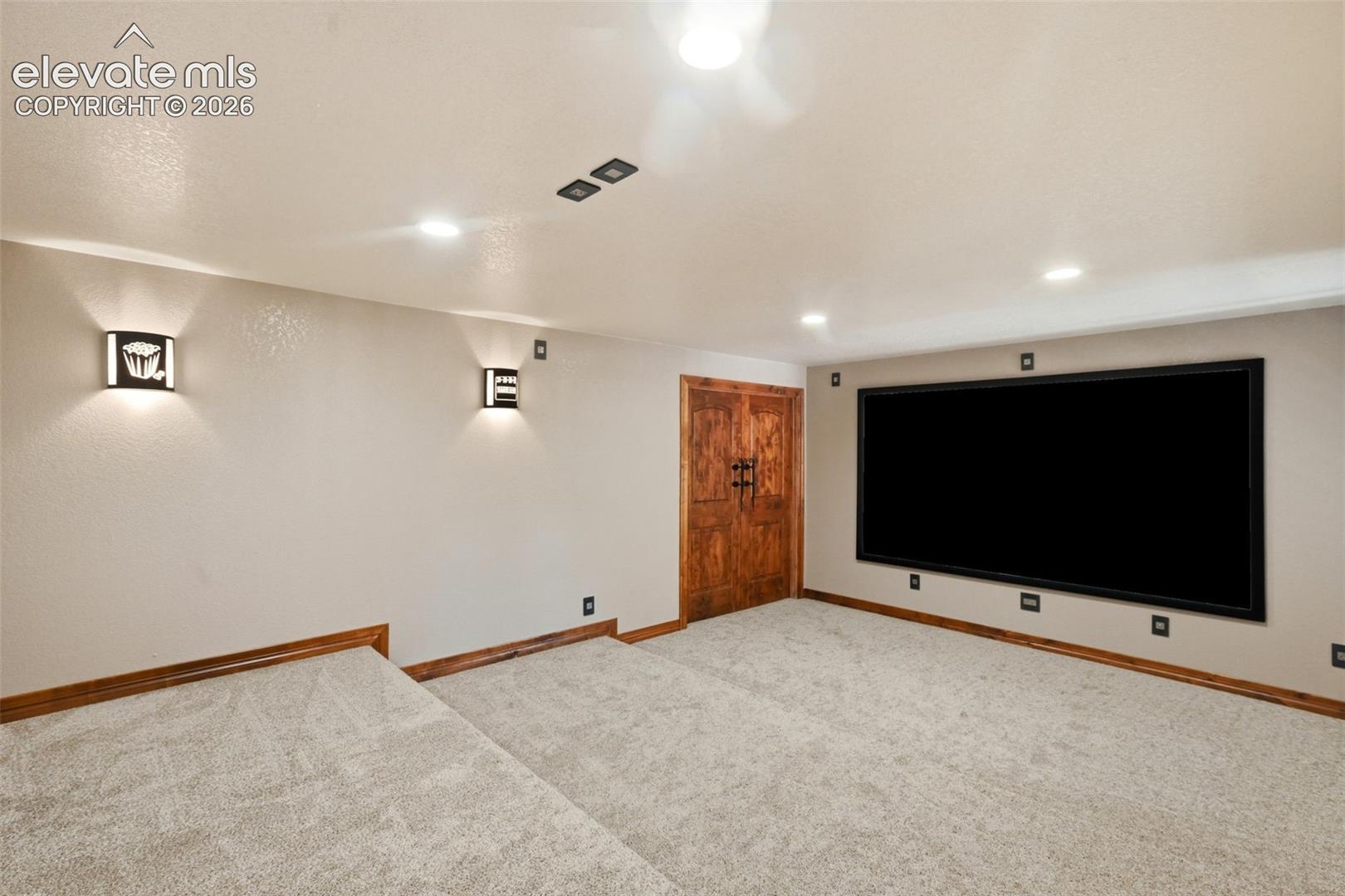 Dedicated media room featuring a large projection screen, tiered carpeting, recessed lighting, and decorative wall sconces