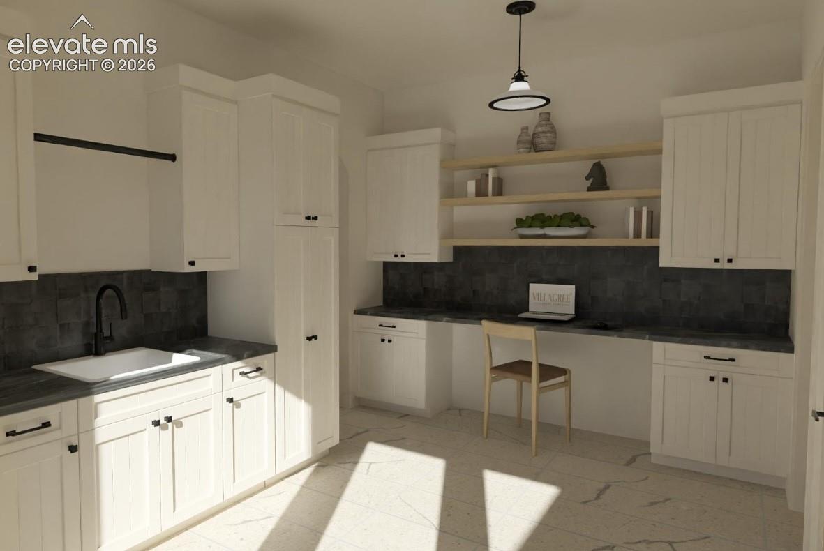White cabinetry with black hardware, integrated sink with a matte black faucet, dark tile backsplash, light-toned flooring, and built-in desk area or bench with wood shelving