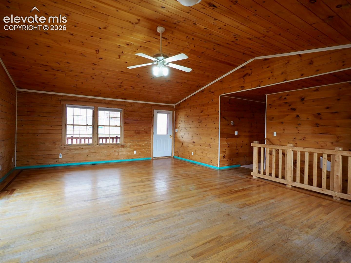 Vaulted wood-paneled ceiling, wood-finish flooring, wood-paneled walls, built-in wooden staircase railing, and ceiling-mounted fan with integrated lighting