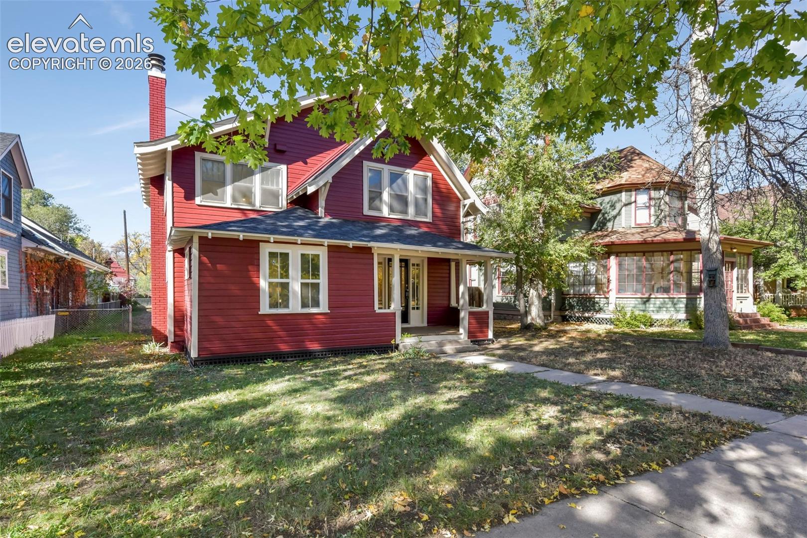 Two-story home with wood lap siding, an exterior chimney, multi-pane windows, and a covered front porch