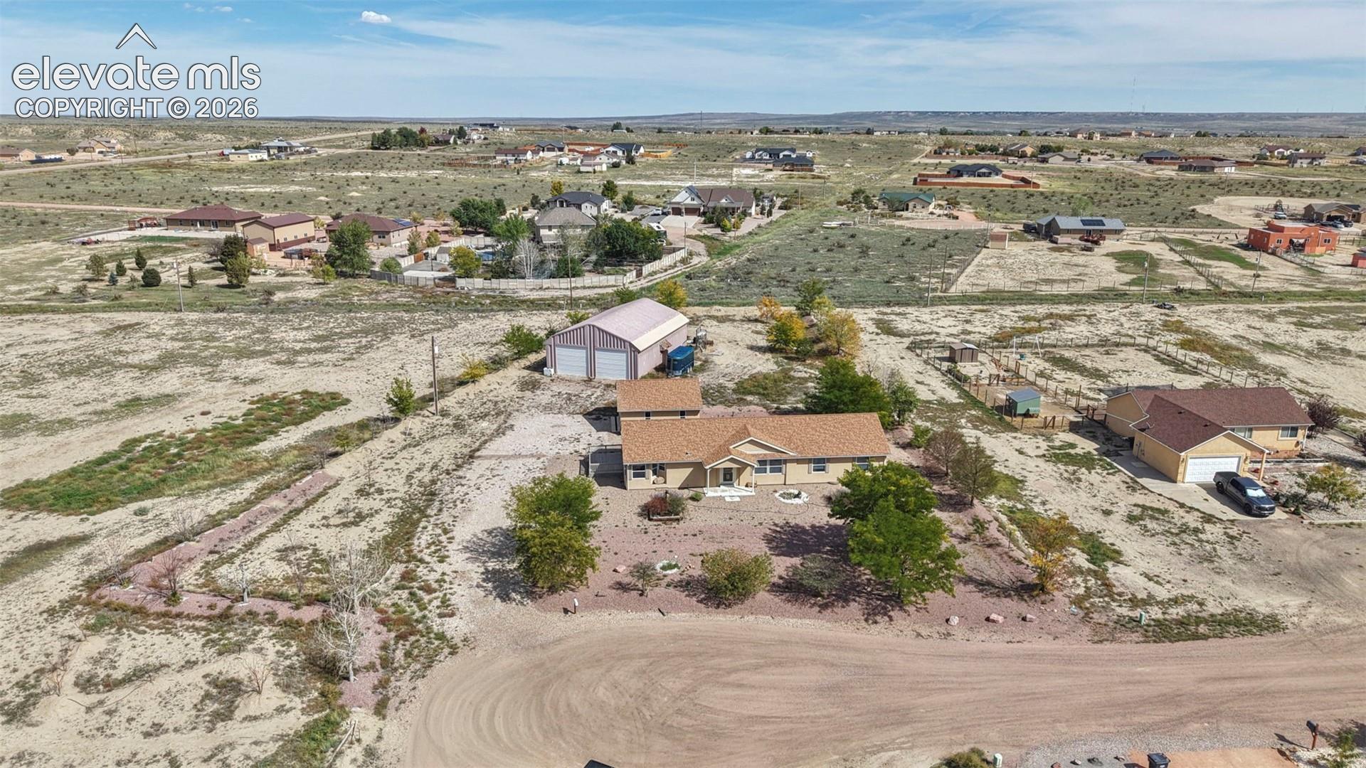 Single-story residence featuring a shingled roof, a detached metal-sided garage, and a sprawling lot with established trees and low-maintenance native landscaping