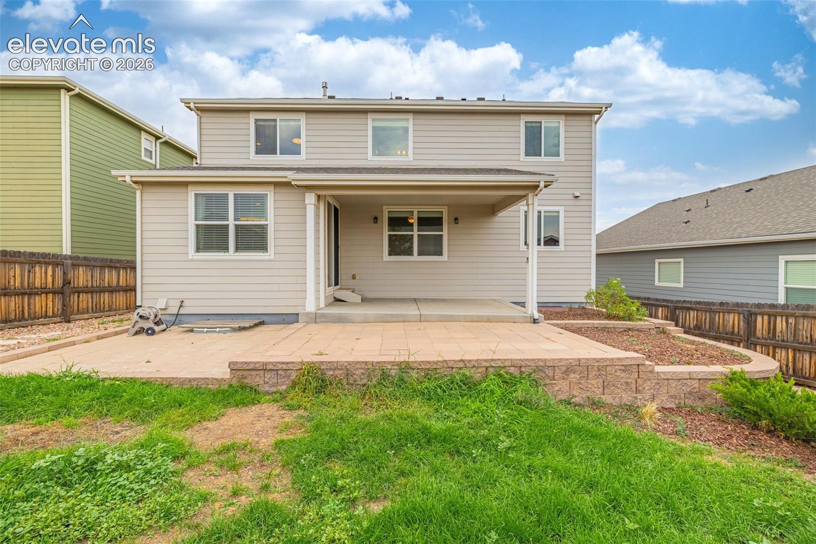 Two-story exterior with horizontal siding, featuring a covered patio, an open patio, and a retaining wall with landscaping