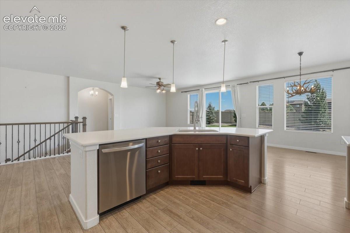 Contemporary kitchen island featuring a stainless steel dishwasher, undermount sink with a gooseneck faucet, light-toned countertop, and rich wood-finish cabinetry