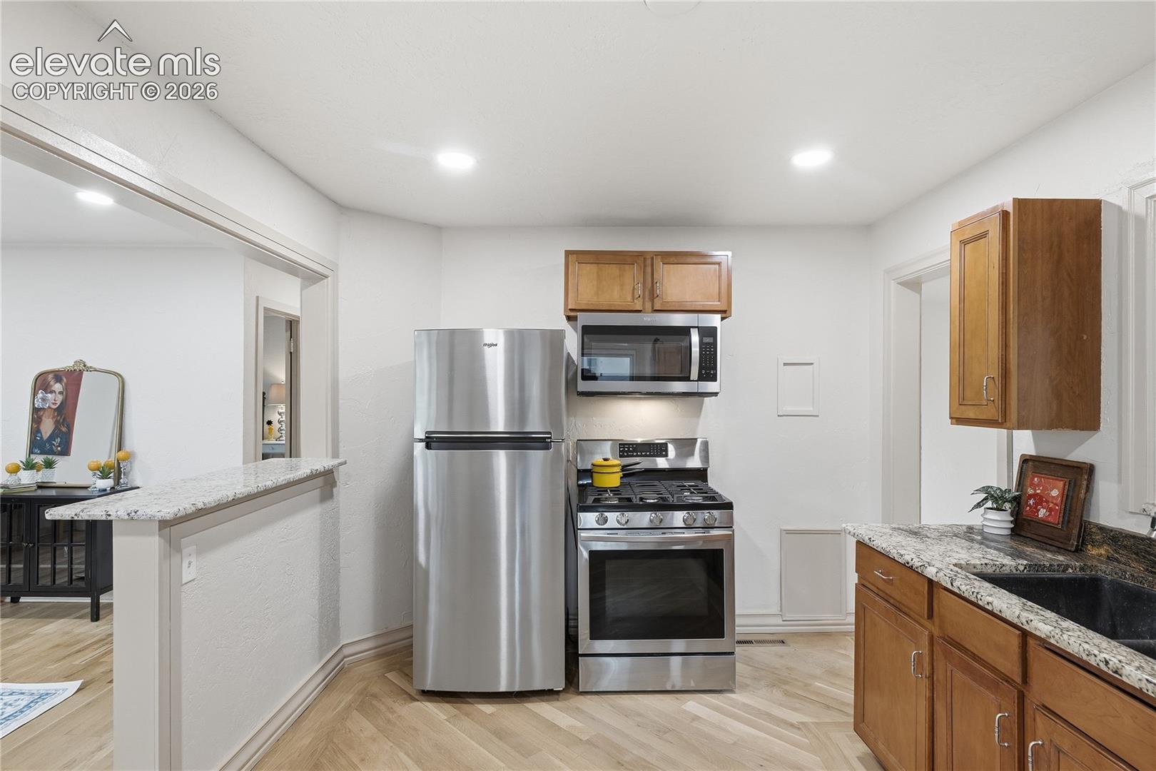 Kitchen featuring wood cabinetry, stone-finish countertops, stainless steel appliances, and herringbone-pattern wood-finish flooring