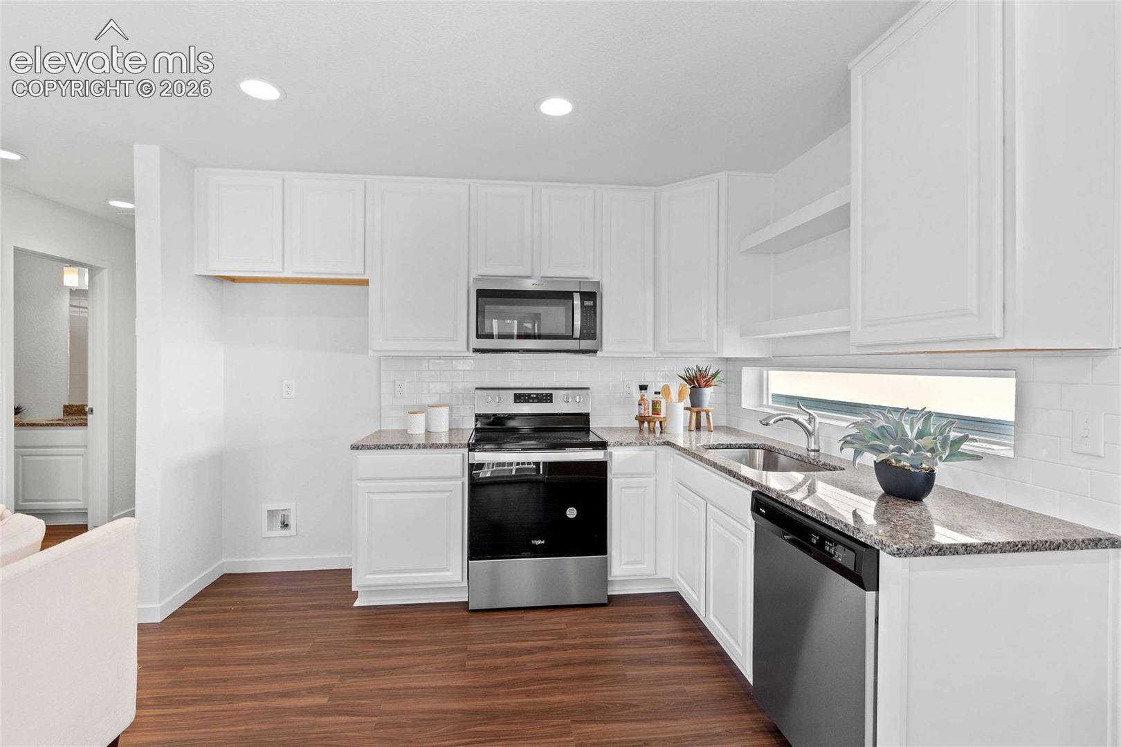 White cabinetry with polished hardware, granite countertops, white subway tile backsplash, stainless steel appliances, and wood-finish flooring
*photos of a model home*