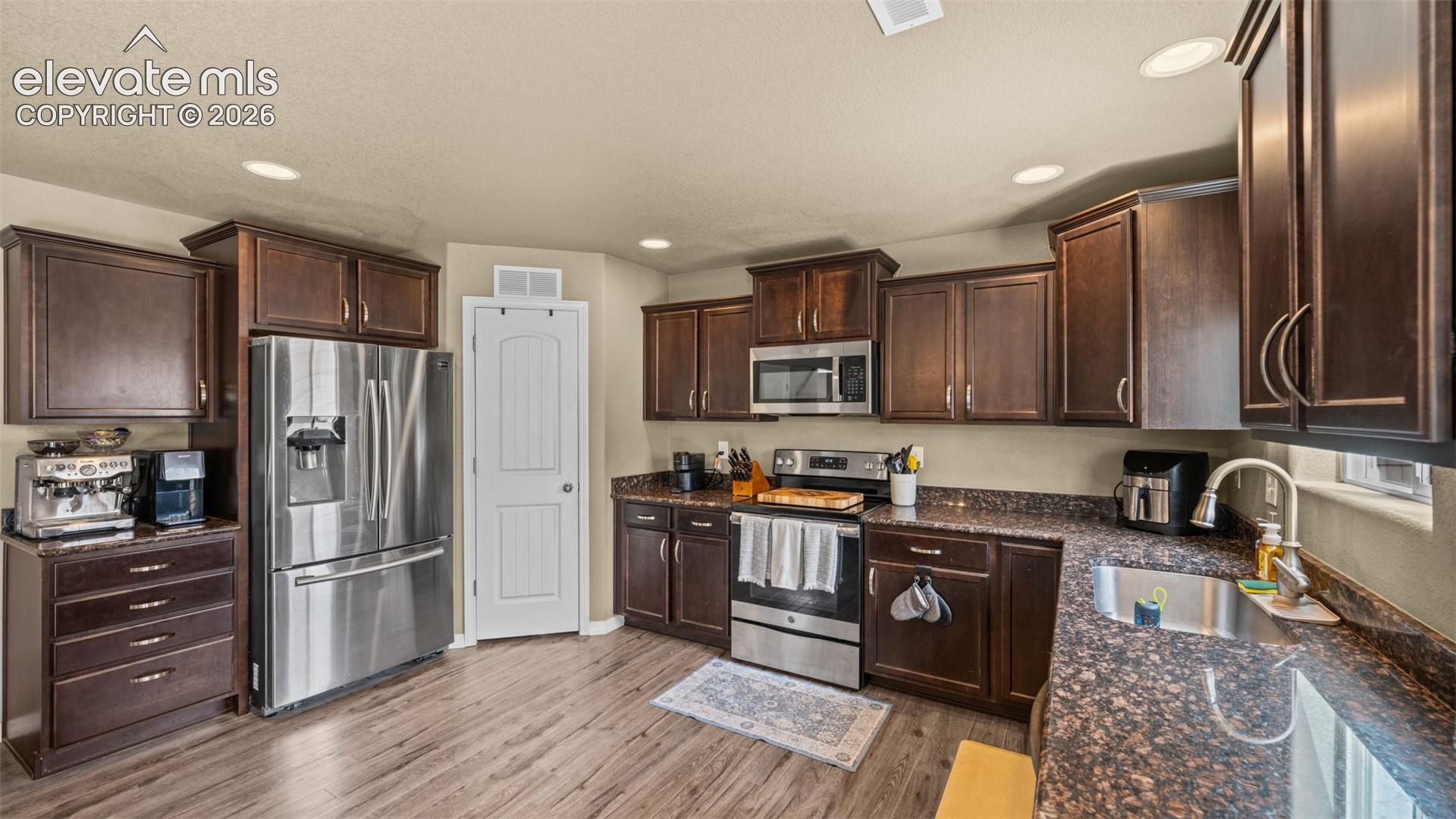 Kitchen featuring wood-finish flooring, dark wood cabinetry, stainless steel appliances, and mottled countertops