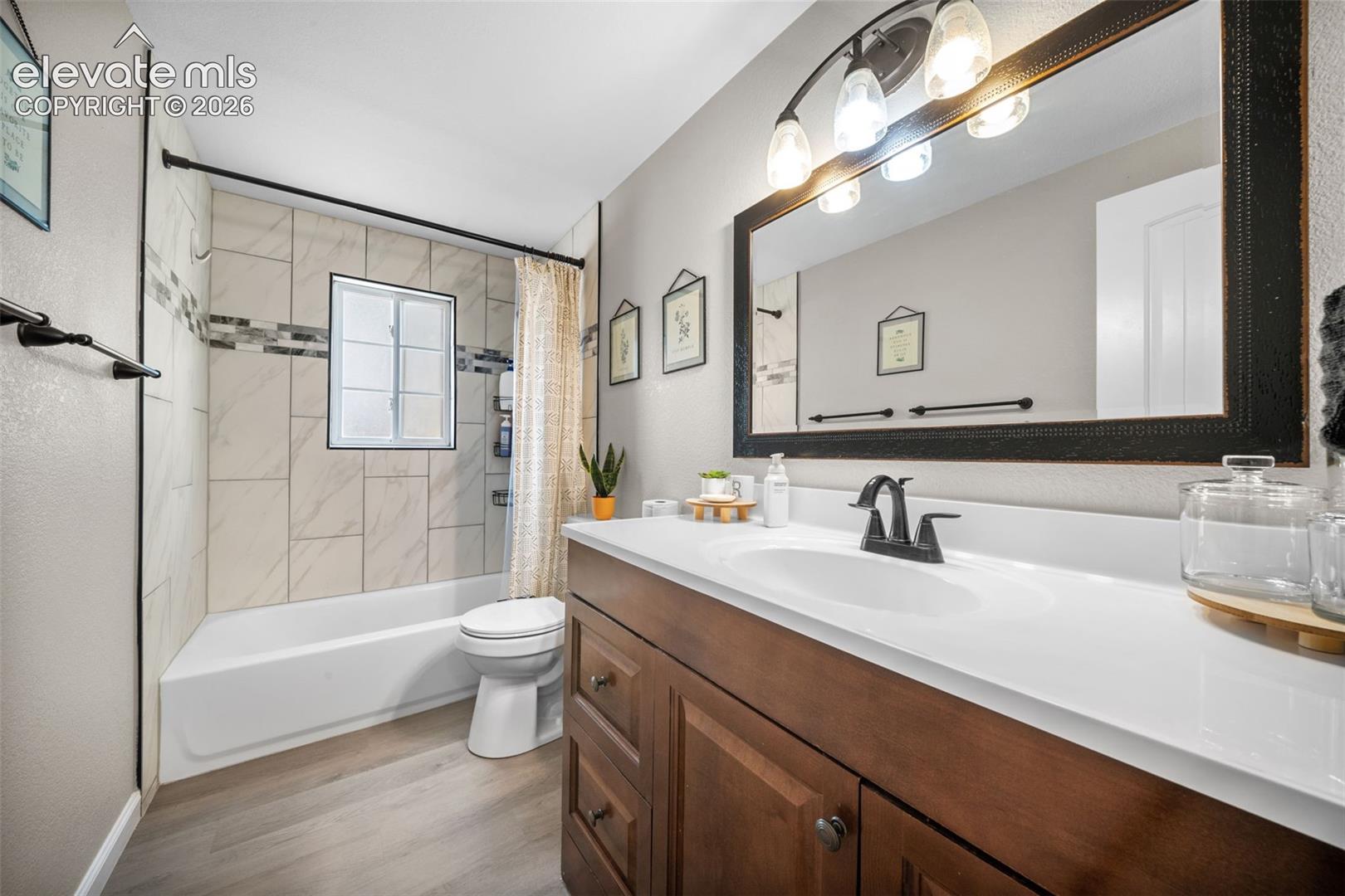 Bathroom featuring a single vanity with wood-finish cabinetry, a white countertop, and a framed mirror with integrated lighting
