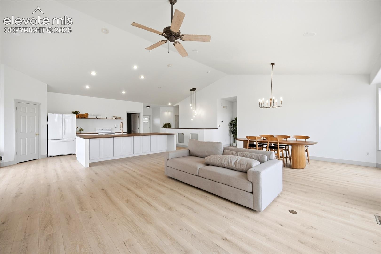 Open-concept interior featuring vaulted ceilings, wood-finish flooring, recessed lighting, a kitchen island with stone countertop, and multi-light chandelier fixtures