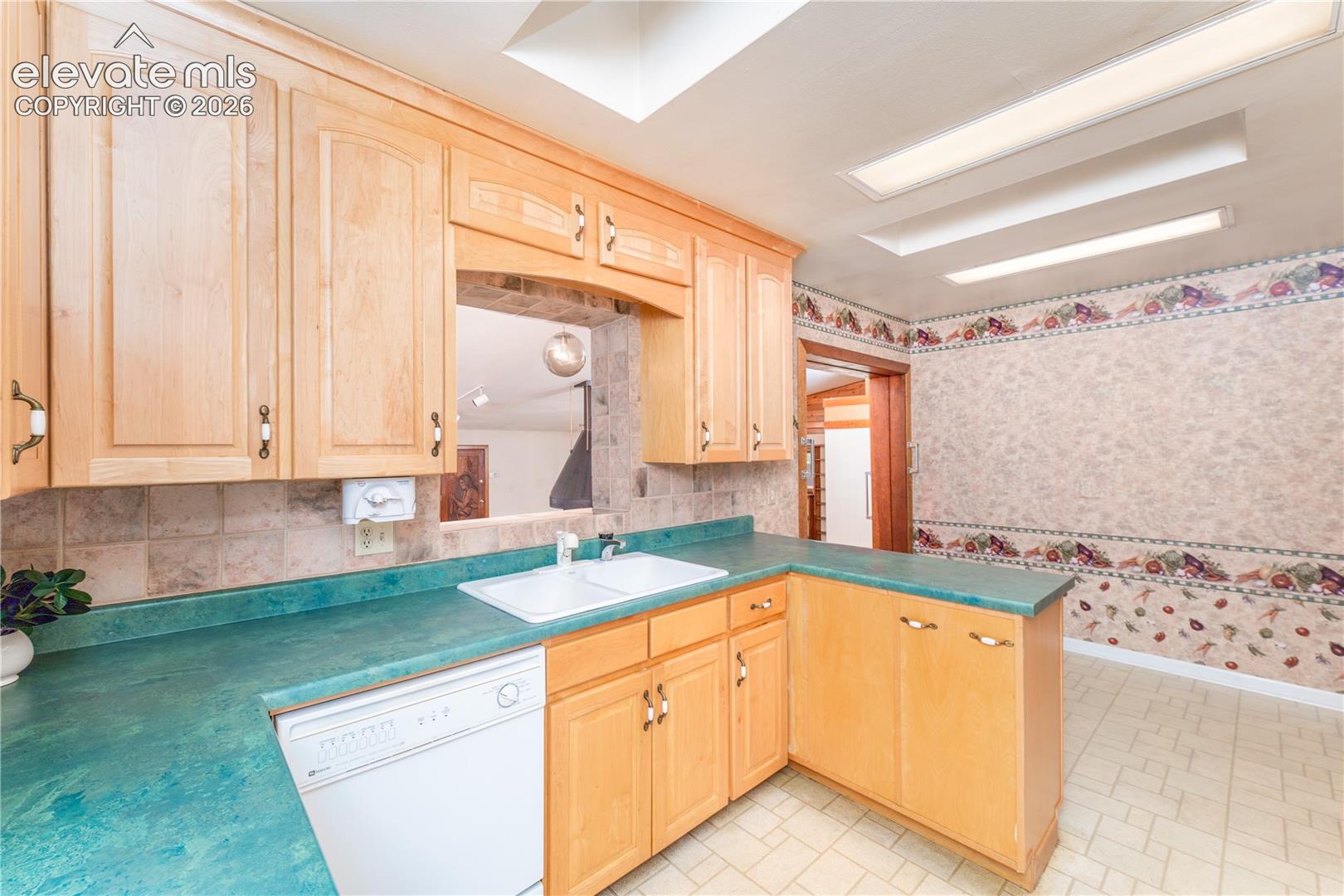 Natural wood cabinetry, a pass-through opening, a dual basin sink, and a dishwasher
