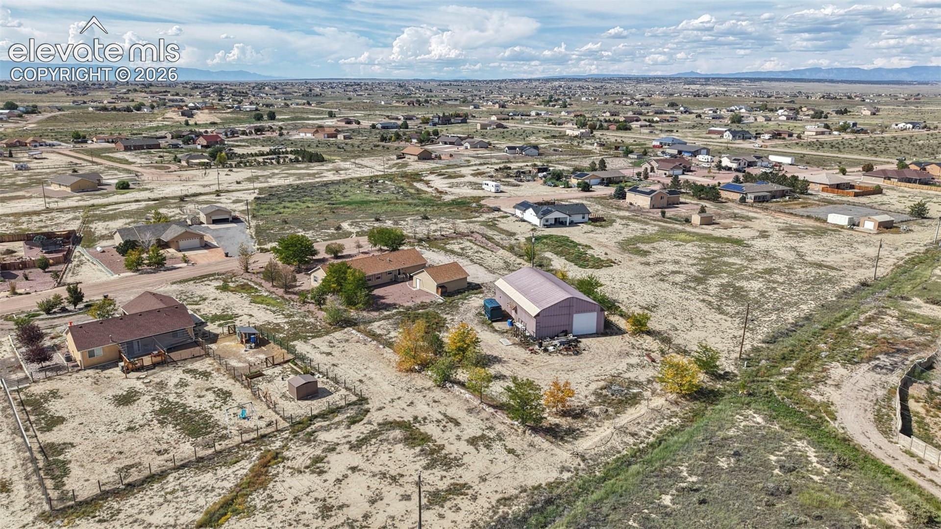 Aerial perspective featuring a detached metal structure, fenced perimeter, and expansive lot