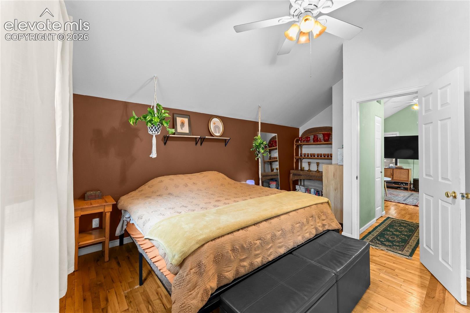 Vaulted ceiling featuring a central lighted ceiling fan, wood-finish flooring, and a six-panel interior door