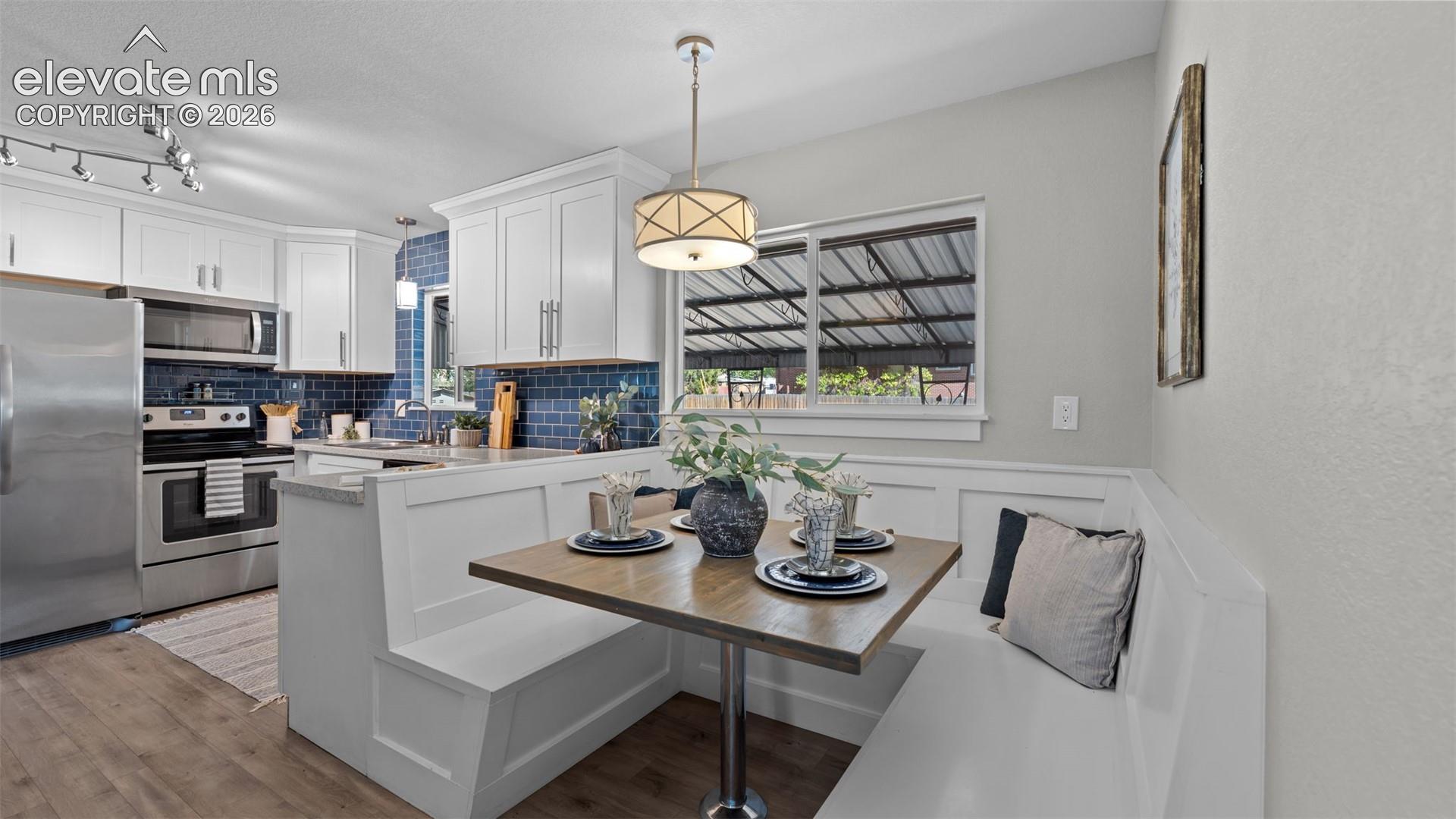White cabinetry, stainless steel appliances, wood-finish flooring, built-in bench seating, and a blue subway tile backsplash