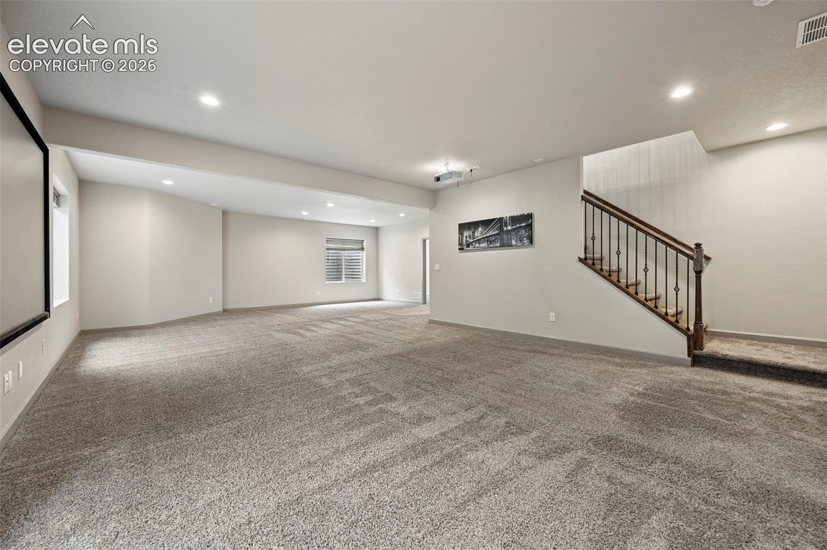 Open-concept area featuring recessed lighting, wall-to-wall carpeting, and a staircase with decorative metal balusters and a wood-finish handrail