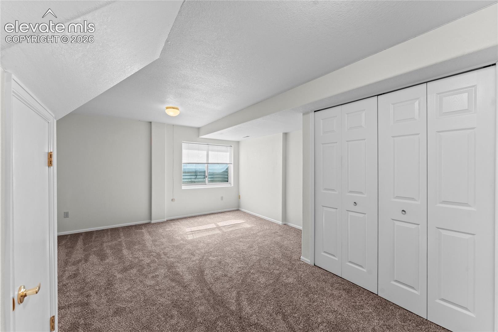 Carpeted room featuring a white interior door, a single window, and bi-fold closet doors