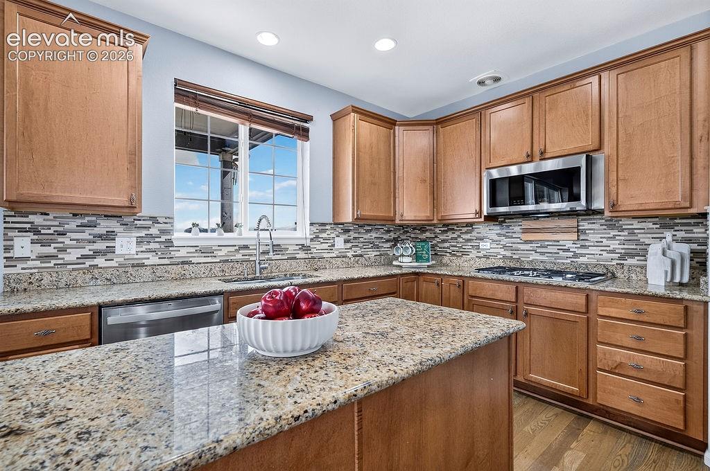 Kitchen featuring wood cabinetry, granite countertops, tile backsplash, stainless steel appliances, and wood-finish flooring