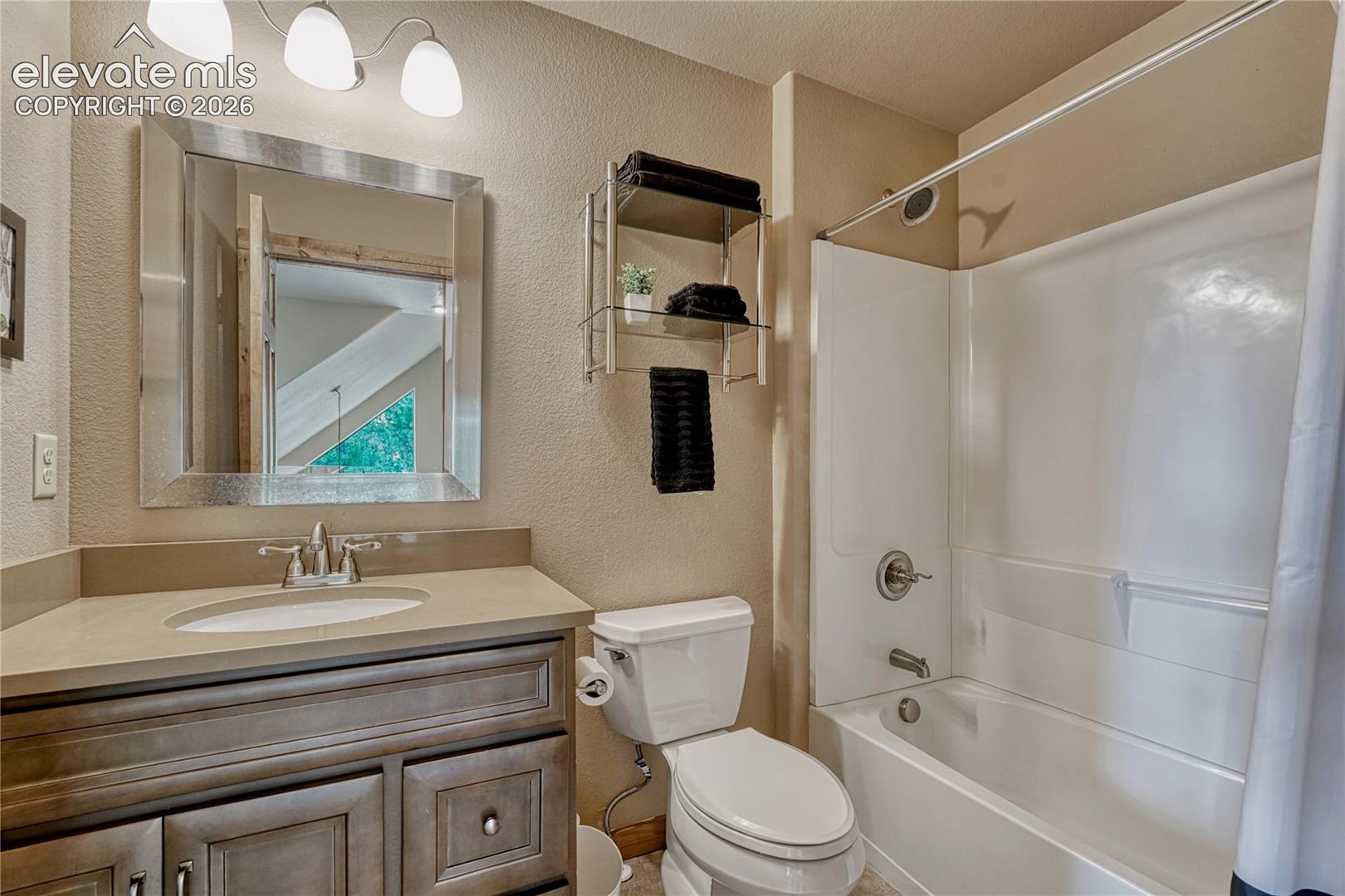 Bathroom featuring a vanity with integrated sink and countertop, framed mirror, three-light fixture, and a tub-shower combination with a surround