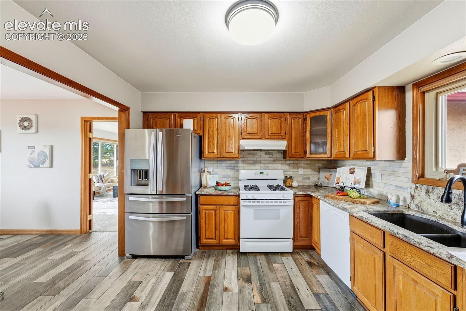 Wood-finish flooring, wood cabinetry, stone countertops, stainless steel refrigerator, and a white gas range