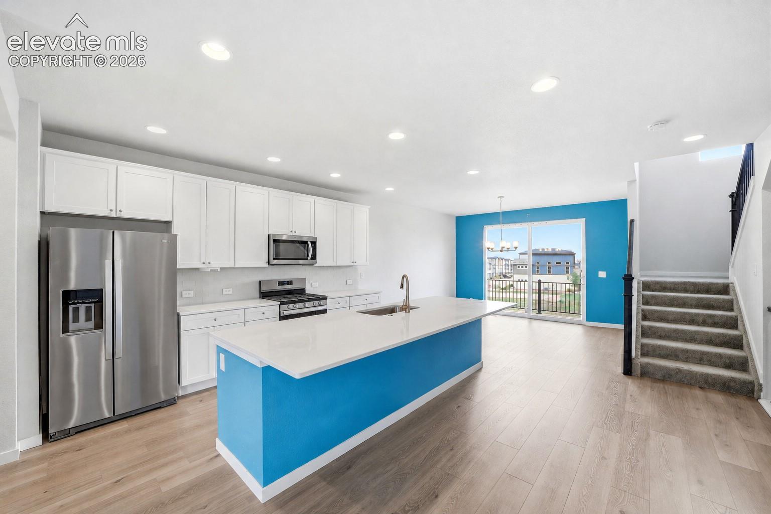 Modern kitchen featuring white cabinetry, stainless steel appliances, a large island with a countertop, wood-finish flooring, and recessed lighting