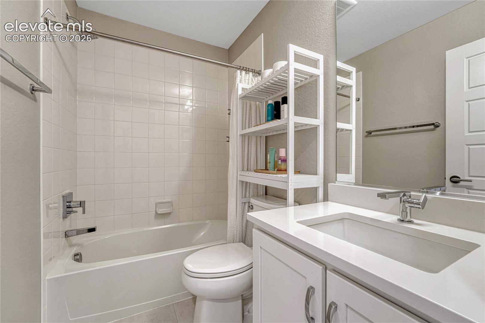 Bathroom featuring a white vanity with a composite countertop and integrated sink, chrome-finish faucet hardware, tub-and-shower combination with full-height wall tiling, and a large-format mirror