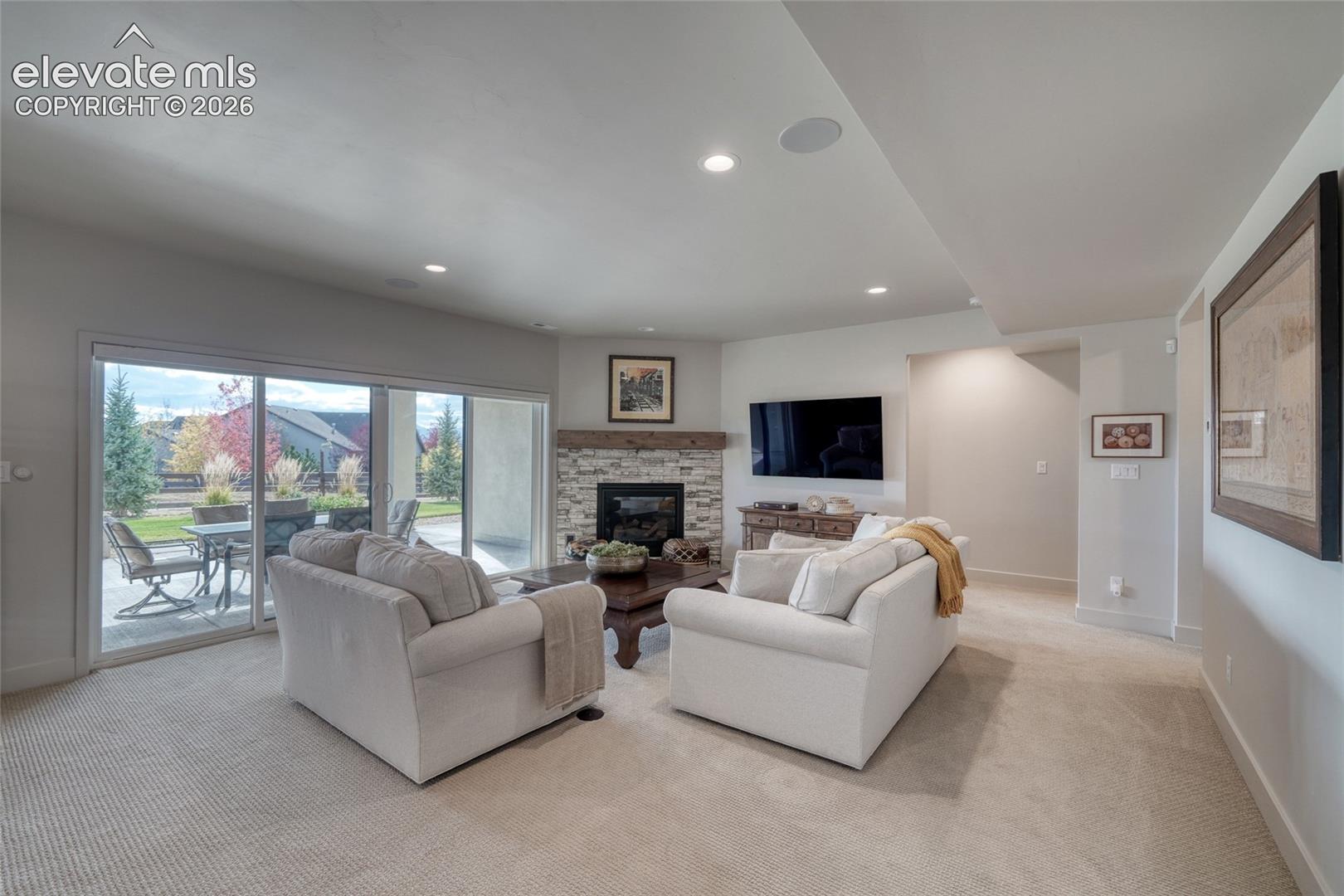Living space featuring carpeted flooring, corner fireplace with stone veneer and wood mantel, recessed lighting, and glass sliding doors