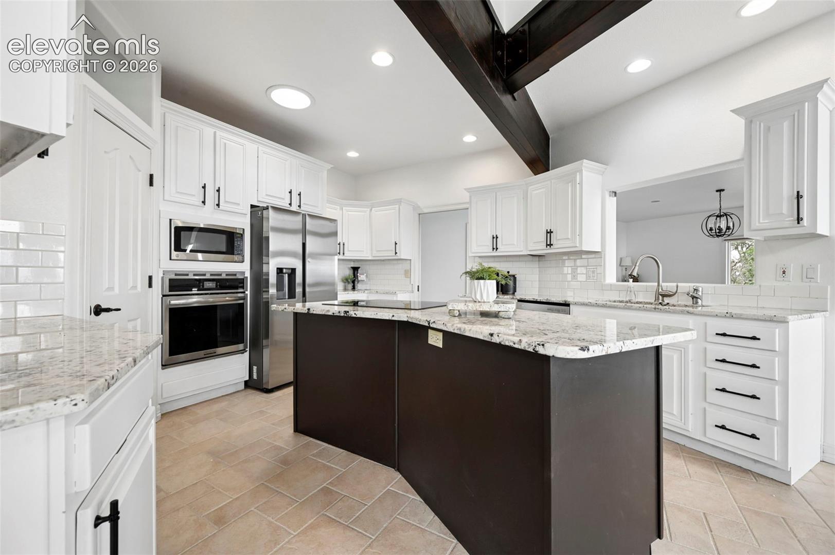 Modern kitchen featuring a central island with a granite countertop, stainless steel appliances, white subway tile backsplash, recessed lighting, and exposed ceiling beams