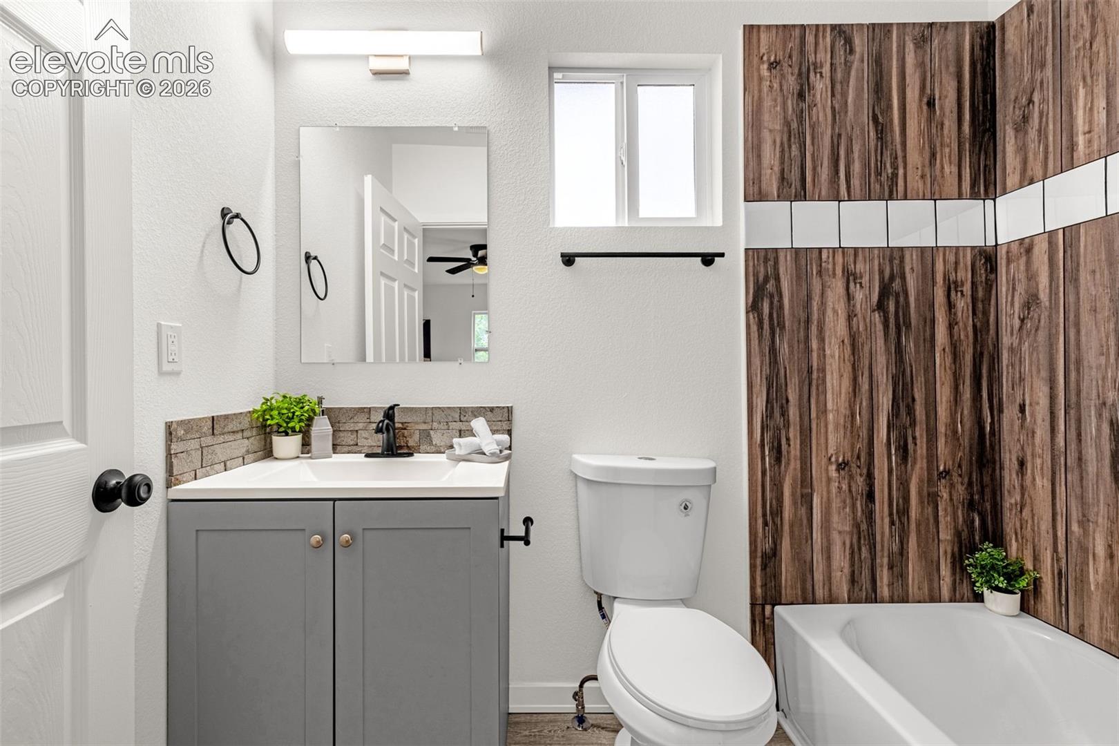 Full bathroom featuring a white bathtub with wood-finish paneling and a tiled accent stripe