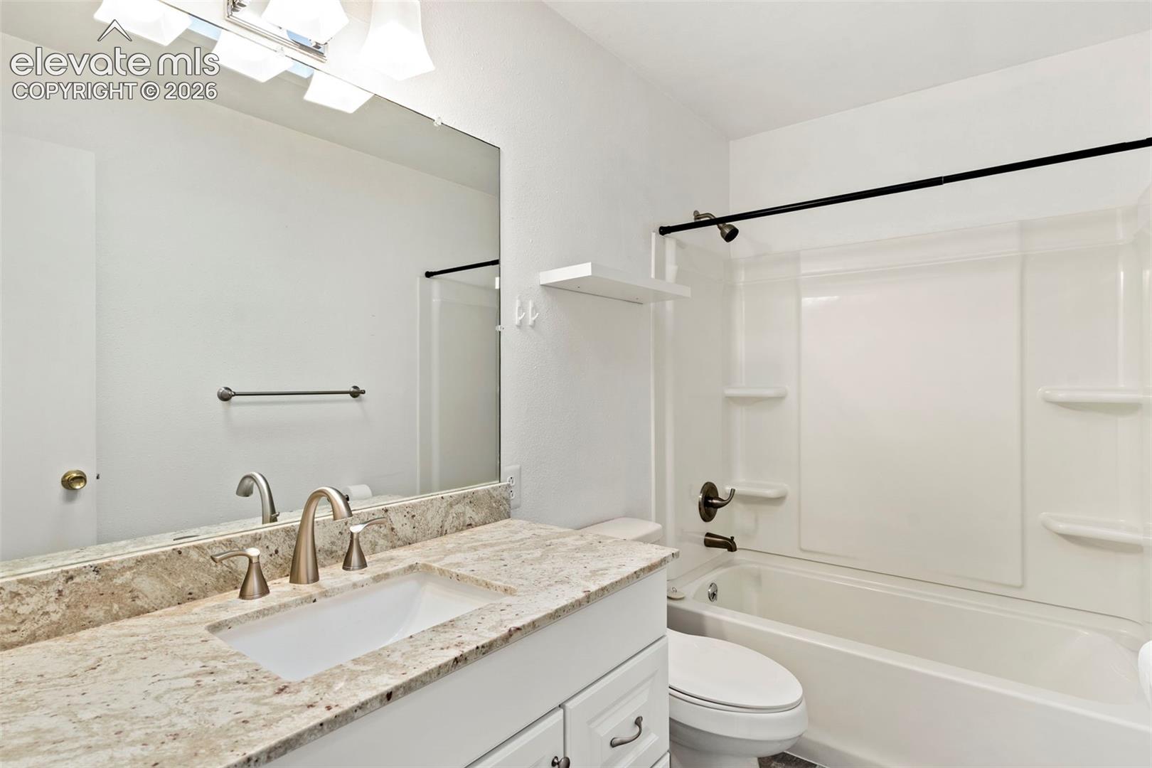 Vanity with integrated sink, stone countertop, brushed nickel faucet, full-width mirror, and white tub/shower combination