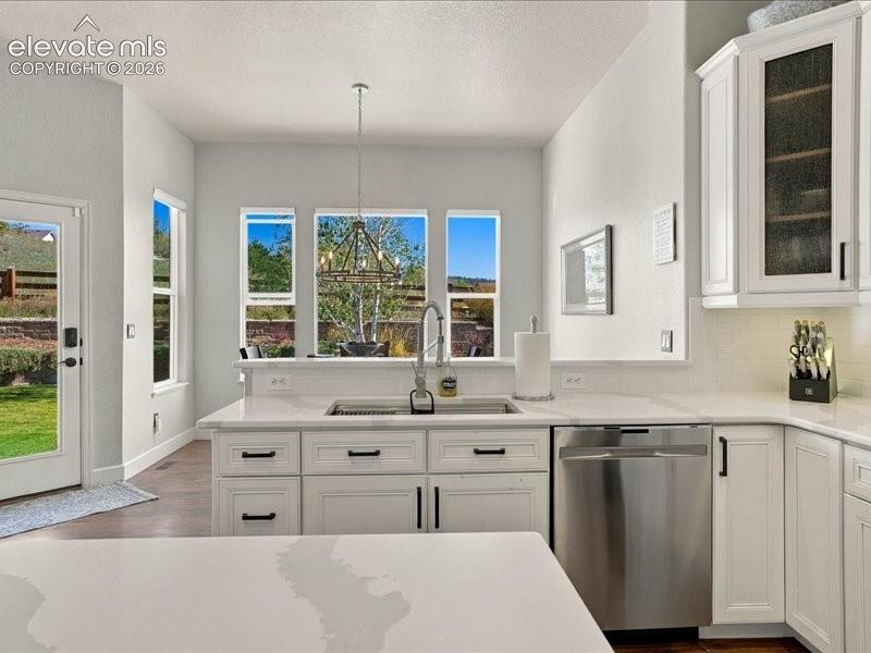Bright kitchen featuring white cabinetry with black hardware, quartz countertops, stainless steel appliances including a dishwasher, and abundant natural light from multi-pane windows overlooking the grounds