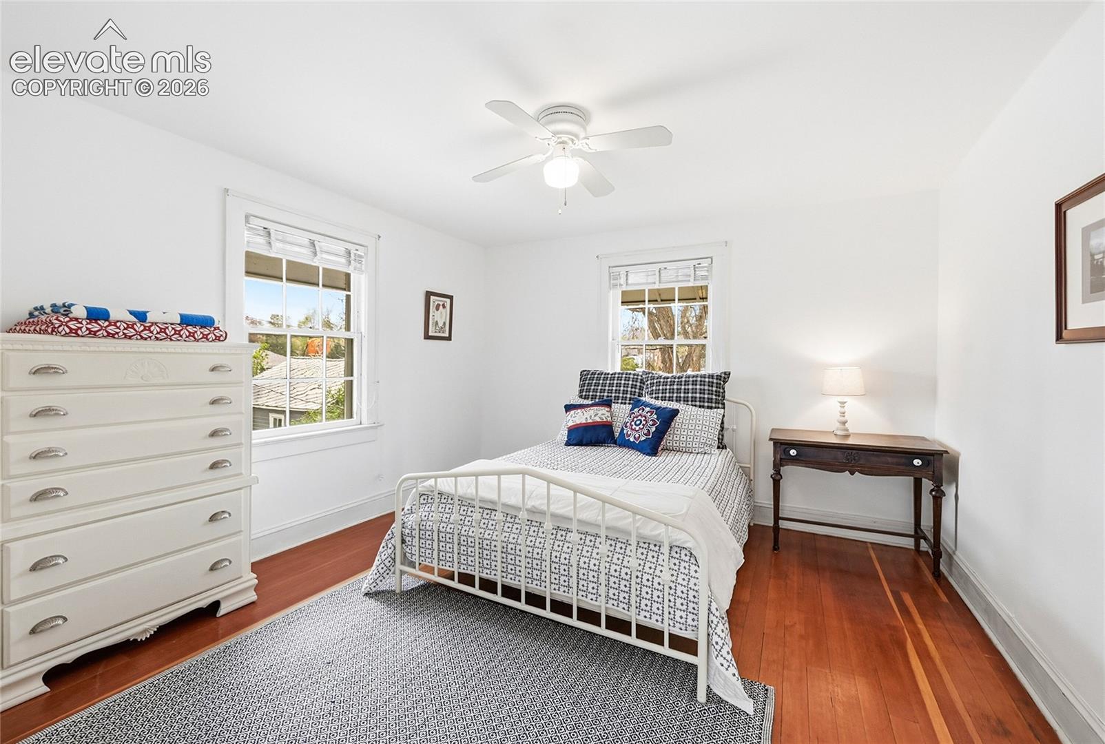 Room featuring wood-finish flooring, two double-hung windows, and a ceiling-mounted light fixture with fan blades