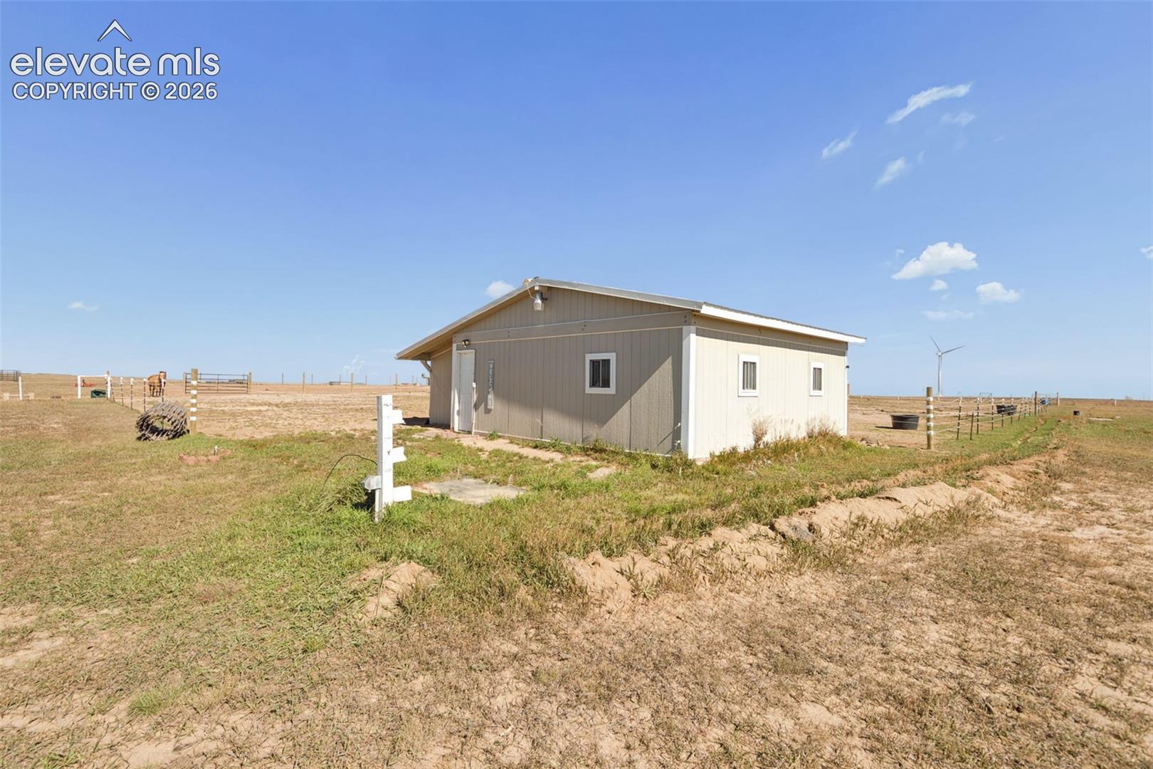 Single-story outbuilding featuring vertical siding, a metal roof, and multiple exterior-access doors, situated on a fenced acreage parcel