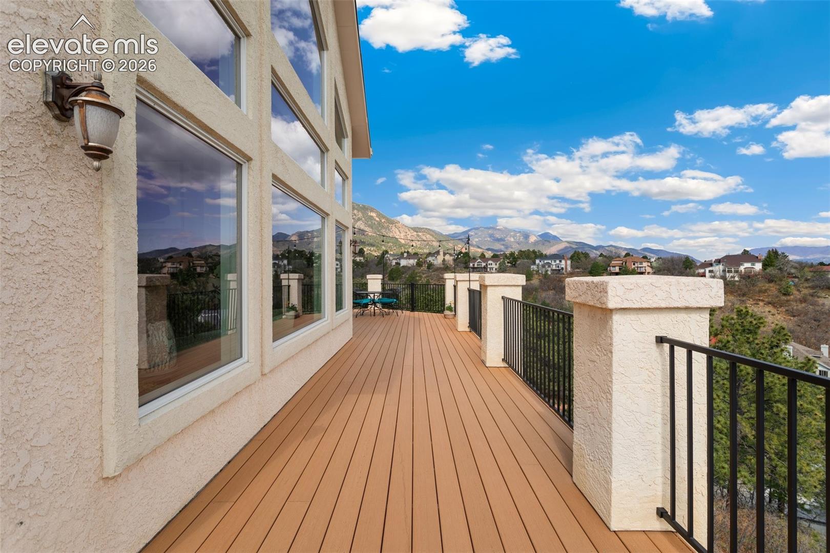 Expansive outdoor deck featuring wood-finish flooring, stucco exterior, and black metal railings