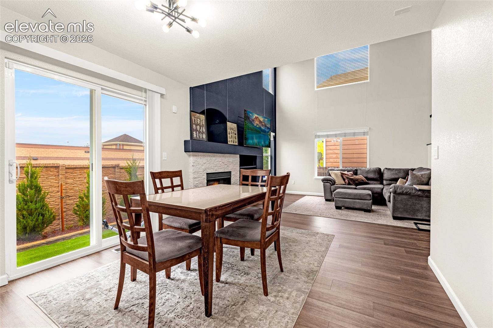 High ceilings, stone-surround fireplace, dark wood-finish flooring, sliding glass door, and modern chandelier