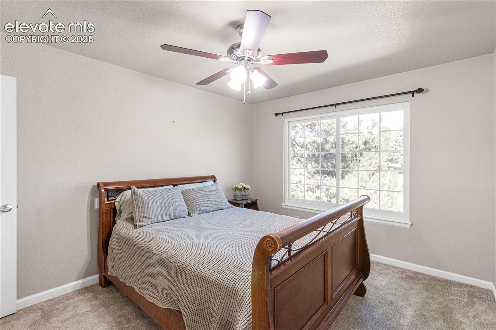 Neutral-toned room featuring a multi-light ceiling fan, large dual-pane window with grid inserts, and wall-mounted curtain rod