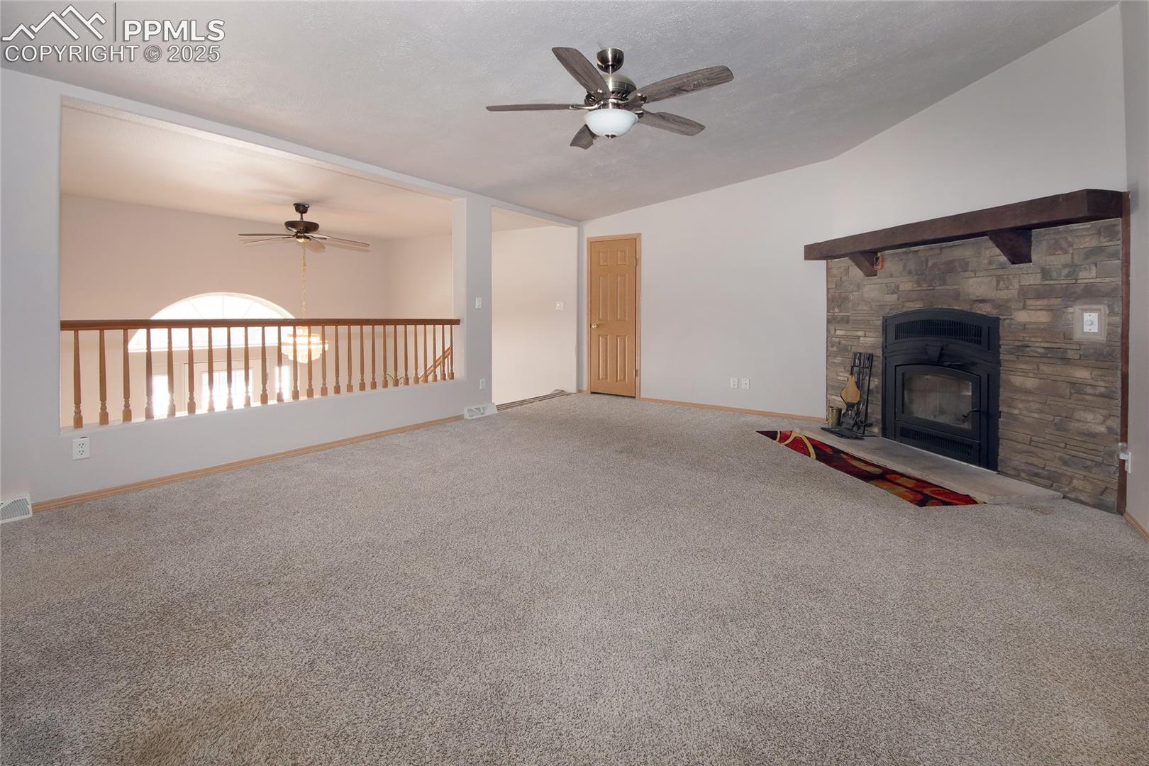 Living room featuring carpet, vaulted ceiling, and a stone fireplace